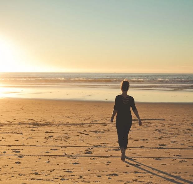 Mulher caminha sozinha na praia ao entardecer, simbolizando calma e controle da ansiedade.