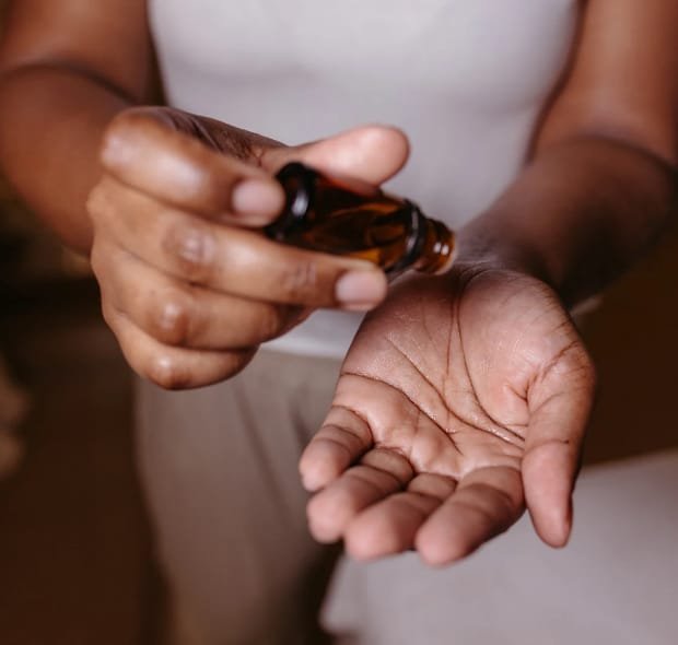 Pessoa aplica óleo essencial de melaleuca na palma da mão, demonstrando o modo de uso do produto.