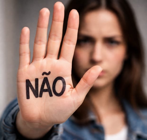 Mulher com a mão estendida para frente, com a palavra ‘não’ escrita na palma, simbolizando limites e assertividade.