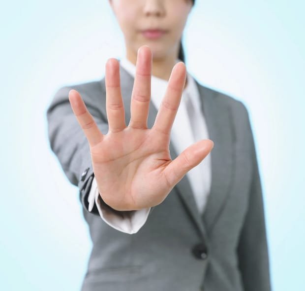 Mulher vestida com roupa social estende a mão aberta em gesto de limite ou sinal de pare, representando a importância de dizer não