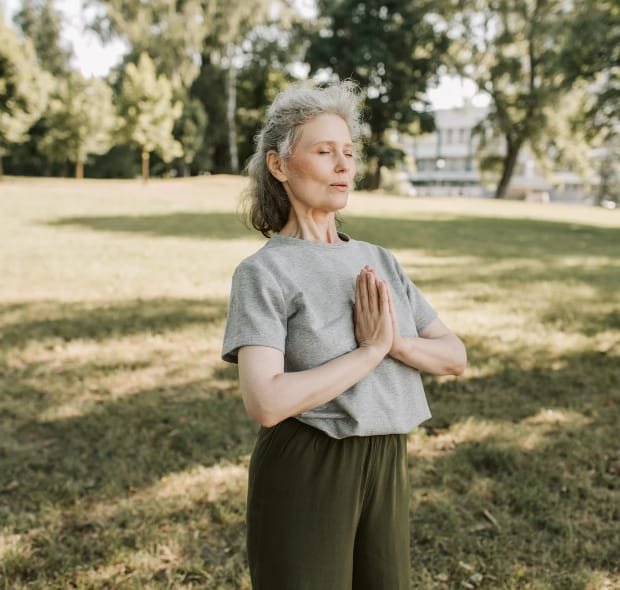 Mulher em área verde pratica respiração consciente para controlar a ansiedade.